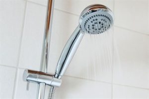A modern shower head pouring water with a white tile background