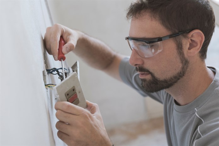 A closeup of an electrician with safety goggles on working with an electrical outlet
