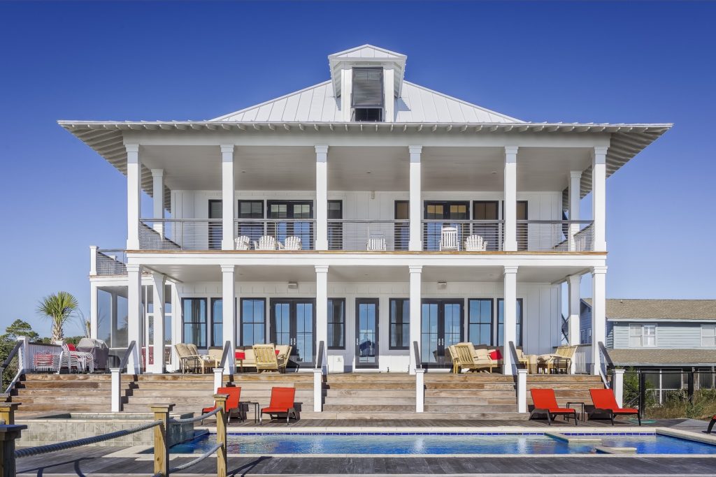 two story white beach house with pool in front and red lounge chairs